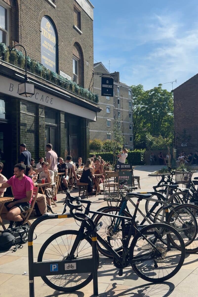 Bikes locked outside a pub on Columbia Road in London while people drink in the sun