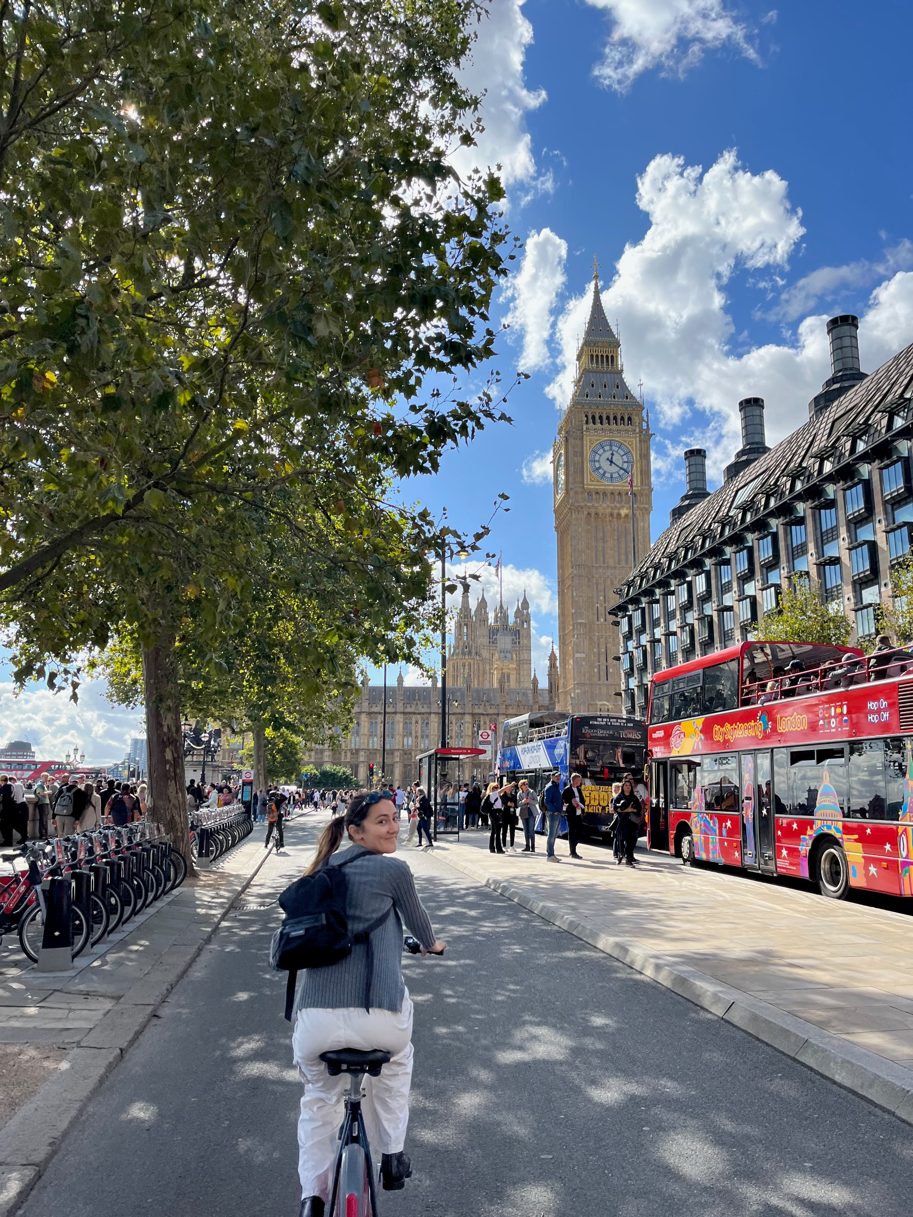 A rider looking back over her shoulder on a cycle track past Big Ben and a row of Santander Cycles docks in London